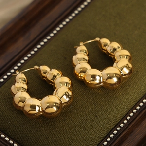 Boucles d'oreilles créoles dorées en forme de U avec texture perlée sur fond sombre