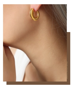 Detail shot of golden C-shaped earrings with ribbed mesh texture on a model ear
