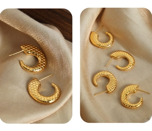 Detailed close-up of golden C-shaped titanium earrings with fish scale and striped textures