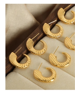 Detail of gold titanium C-shaped earrings with honeycomb and radial mesh texture