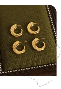 Macro detail of gold C-shaped earrings with mesh and snake scale textures on green fabric