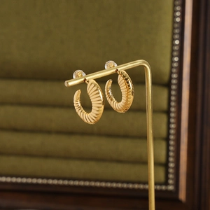 Golden C-shaped textured earrings with ribbed pattern displayed on jewelry stand