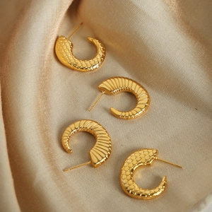 Gold C-shaped hoop earrings set with honeycomb and radial textures on silk background