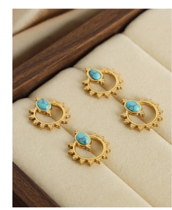 Close-up of four sunburst gold earrings with turquoise stones in a beige velvet jewelry box