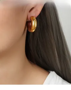 Close-up of a wide C-shaped gold-plated earring with brown enamel on a female model