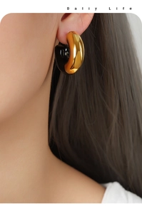 Close-up of model wearing gold and black enamel C-shaped hoop earrings with a glossy finish