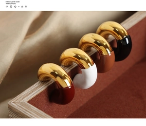 Close-up of C-shaped gold-plated hoop earrings with colorful enamel in four elegant colors
