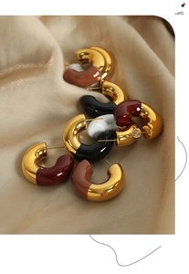 Detailed close-up of C-shaped 18k gold plated enamel earrings on champagne silk fabric