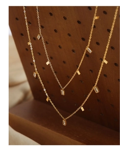 Detalle de gargantilla de titanio dorado con dijes de circón en soporte de madera