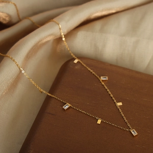 Elegante collar de acero de titanio dorado con colgantes de circón sobre soporte de madera