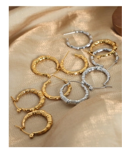 Macro detail of gold and silver bamboo texture hoop earrings on silk background
