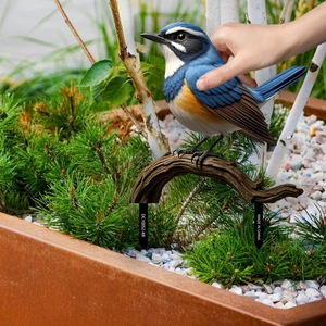 Detail of blue bird garden stake with feather texture on a wooden-style branch base