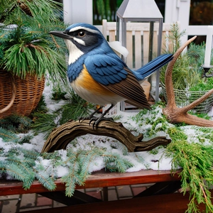 Realistic colorful bird figurine on resin branch amidst snow and pine garden decor
