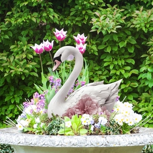 Elegant white swan garden ornament with pink floral accent placed in a lush flower bed