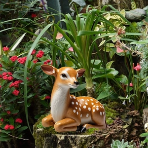 Detailed close-up of a lifelike spotted deer garden ornament resting in green foliage
