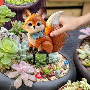 Detail of cartoon fox garden stake with blue bow placed in a succulent planter