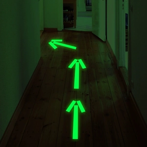 Lichtgevende groene pijlstickers op donkere houten vloer voor veiligheidsgeleiding in huis