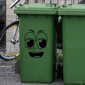 Grappige cartoon glimlachend gezicht sticker aangebracht op een groene vuilnisbak