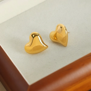 Asymmetric heart-shaped gold studs in a jewelry box with polished stainless steel finish