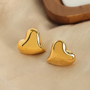 Asymmetrical gold heart stud earrings on champagne silk background with wood tray