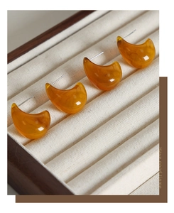 Macro shot of amber resin droplet earrings with crescent moon design on velvet display