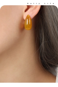 Detail of tear-drop yellow resin earring on model with elegant gold-plated steel finish