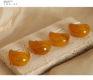 Detail of amber resin teardrop earrings on beige stone stand with silk fabric