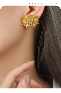 Macro shot of gold sunflower earrings with leaf texture and embedded zircon stones