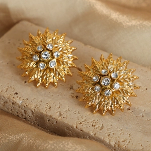 Elegant gold sunburst earrings with leaf texture and zircon stones on a stone base