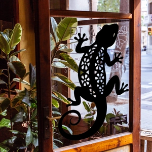 Close-up of a black gecko wall sticker with floral patterns on a glass shop door