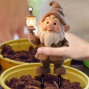 Close-up of a cute garden gnome stake with a lantern being placed into a flower pot