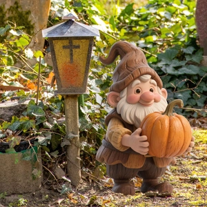 Detail of garden gnome statue holding orange pumpkin in a natural outdoor garden setting