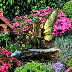 Detail of magical green fairy ornament sitting on stone base with vintage lantern in garden