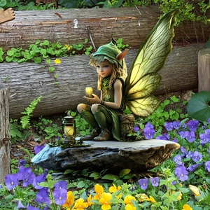 Garden fairy statue with green wings and glowing lantern among pansy flowers