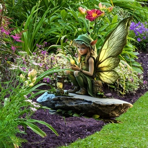 Detailed close-up of a green forest fairy statue with wings and lantern in garden