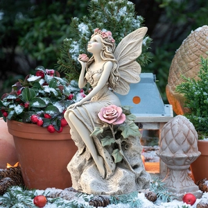 Close-up of a garden fairy statue with detailed wings and roses in a snowy winter setting