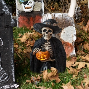 Detail of Halloween skeleton with wizard hat holding a glowing pumpkin lamp on lawn