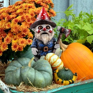 Creepy garden gnome clown statue with bloody axe among pumpkins and autumn harvest decor