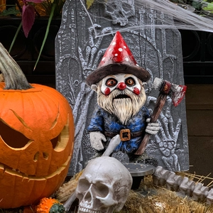 Creepy Halloween gnome statue holding a bloody axe with pumpkin and skull background