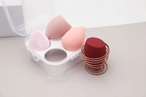 Detail of four colorful makeup sponges with a drying rack and transparent storage box