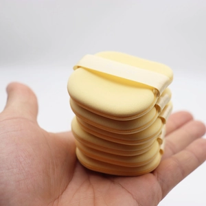 Hand holding six soft butter yellow makeup puffs with Buffer ribbon detail and sponge texture
