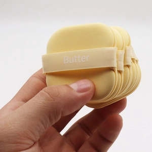 Close-up of soft square butter makeup sponges with yellow ribbon handles in hand