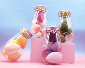 Detail of colorful makeup sponges in daisy lid bottles on a pink geometric platform