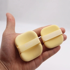 Detail of soft yellow rectangular butter puff makeup sponges with branded ribbon handle
