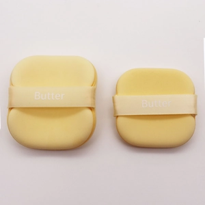 Macro shot of two soft yellow butter makeup sponges with satin ribbons on white background