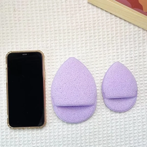 Dettaglio macro di spugne per il trucco viola a goccia in due dimensioni su tessuto bianco