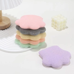 Detail of flower-shaped facial cleansing sponges in six Morandi colors on a minimalist desk