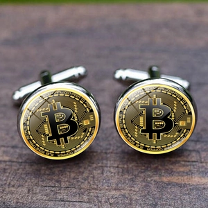 Polished silver Bitcoin cufflinks with black and gold coin design on a wood background