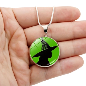 Halskette mit Hexen-Silhouette und grünem Hintergrund an silberner Kette in der Hand