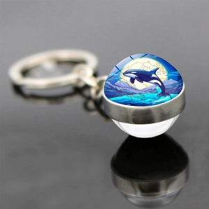 Detailed close-up of a double-sided glass orb keychain featuring an artistic orca whale print